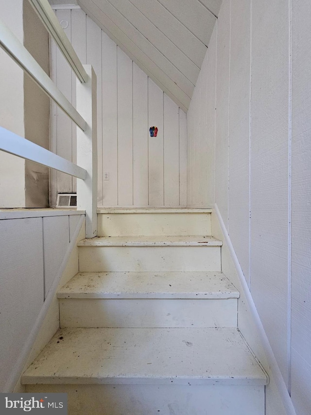 stairway with lofted ceiling and wooden walls