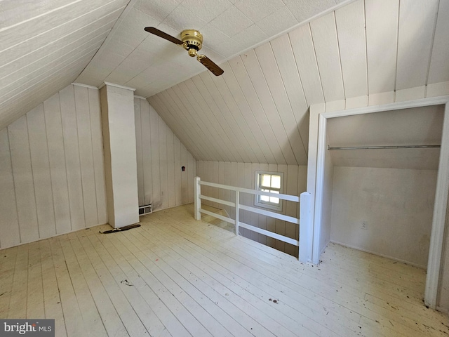 additional living space with light hardwood / wood-style floors, vaulted ceiling, wooden walls, and ceiling fan