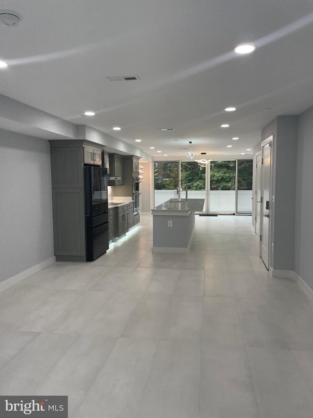 kitchen with a kitchen island, gray cabinetry, sink, stainless steel double oven, and black fridge