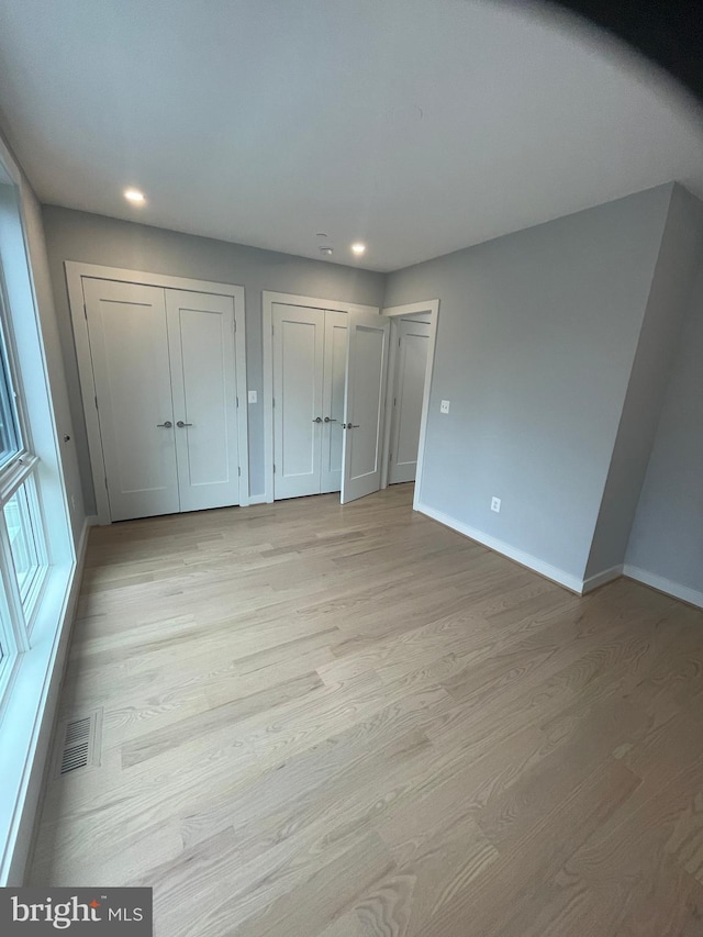 unfurnished bedroom featuring light wood-type flooring and two closets