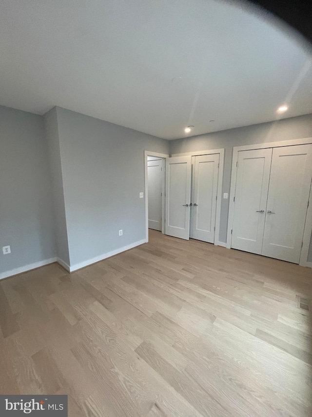 unfurnished bedroom featuring light hardwood / wood-style flooring and two closets