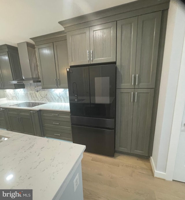 kitchen with light hardwood / wood-style flooring, light stone countertops, wall chimney range hood, black appliances, and tasteful backsplash