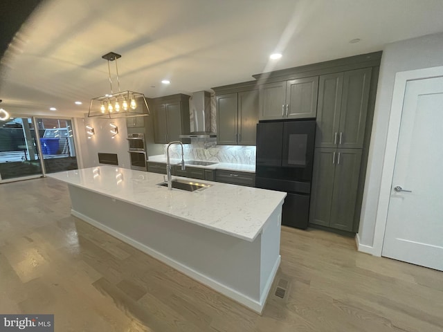 kitchen featuring decorative light fixtures, wall chimney exhaust hood, light hardwood / wood-style flooring, sink, and black refrigerator