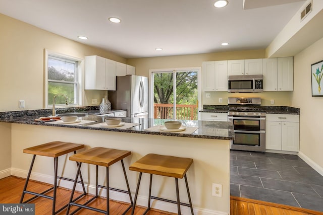 kitchen featuring dark hardwood / wood-style flooring, kitchen peninsula, stainless steel appliances, and white cabinets