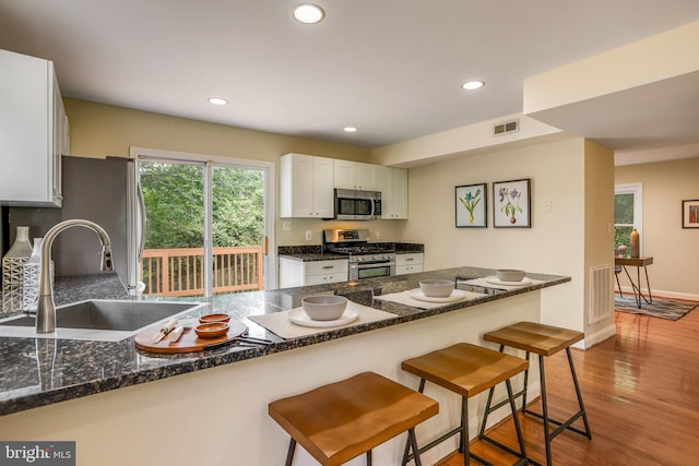 kitchen featuring hardwood / wood-style flooring, stainless steel appliances, white cabinetry, sink, and a kitchen bar