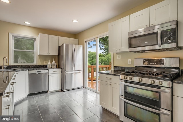 kitchen featuring dark stone counters, dark tile patterned flooring, sink, appliances with stainless steel finishes, and white cabinets