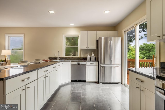 kitchen with stainless steel appliances, sink, dark stone counters, and white cabinets