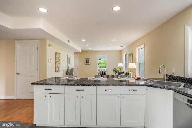 kitchen with light wood-type flooring, dark stone counters, sink, white dishwasher, and white cabinets