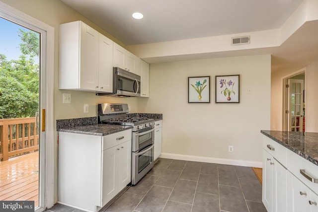 kitchen featuring dark stone countertops, appliances with stainless steel finishes, white cabinetry, and dark tile patterned flooring