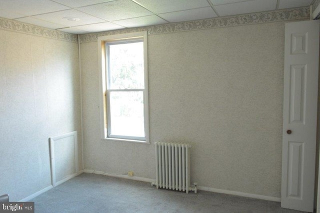 empty room with a paneled ceiling, radiator, and carpet floors