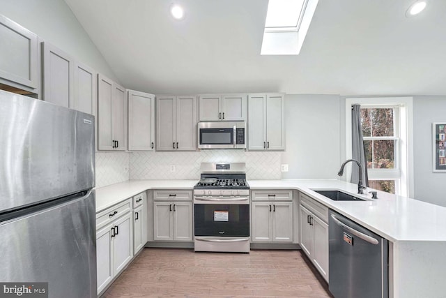 kitchen with kitchen peninsula, light hardwood / wood-style flooring, sink, vaulted ceiling with skylight, and stainless steel appliances