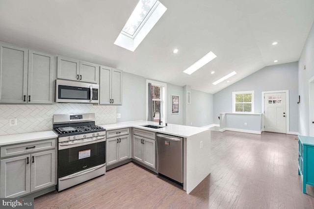 kitchen featuring appliances with stainless steel finishes, sink, kitchen peninsula, vaulted ceiling, and light hardwood / wood-style flooring