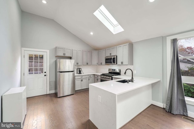 kitchen featuring hardwood / wood-style flooring, kitchen peninsula, stainless steel appliances, sink, and tasteful backsplash