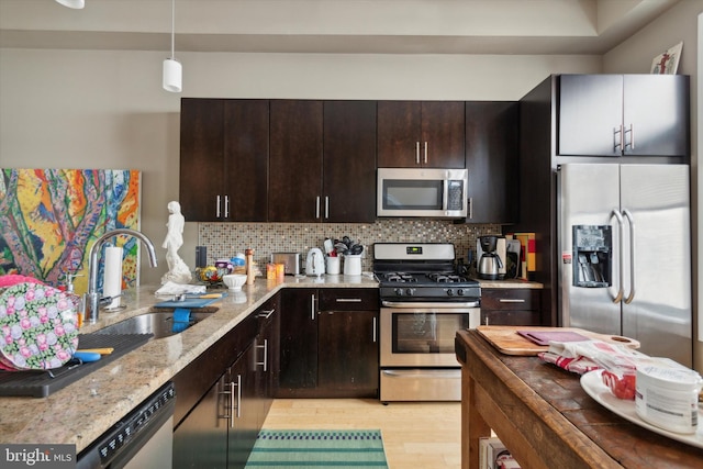 kitchen with tasteful backsplash, light hardwood / wood-style flooring, sink, light stone countertops, and appliances with stainless steel finishes