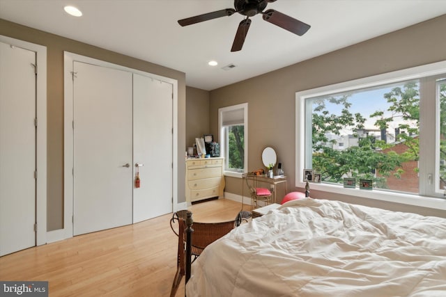 bedroom with light hardwood / wood-style flooring, ceiling fan, and multiple closets