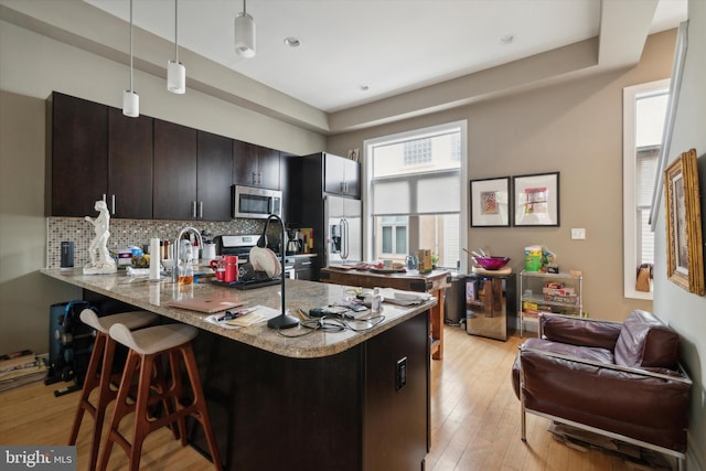 kitchen featuring pendant lighting, light hardwood / wood-style floors, a kitchen bar, stainless steel appliances, and kitchen peninsula