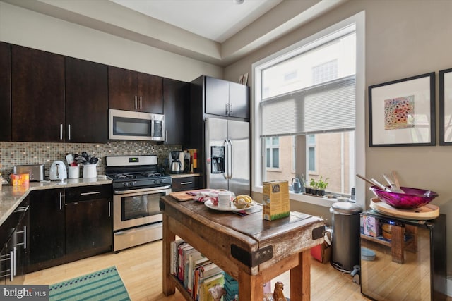 kitchen with light wood-type flooring, backsplash, light stone counters, appliances with stainless steel finishes, and dark brown cabinetry