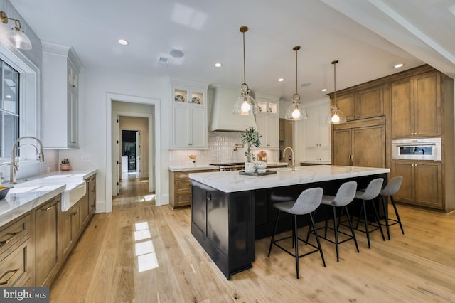 kitchen featuring a spacious island, light hardwood / wood-style flooring, sink, custom range hood, and white cabinets