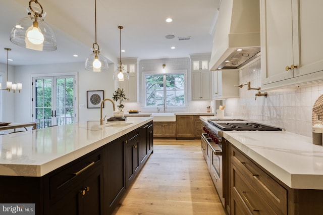 kitchen with a wealth of natural light, an island with sink, decorative light fixtures, and premium range hood