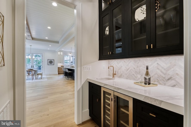 bar with light wood-type flooring, a chandelier, beverage cooler, sink, and light stone countertops