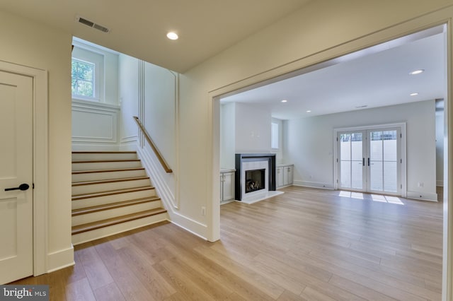 unfurnished living room with light wood-type flooring, french doors, a premium fireplace, and a wealth of natural light