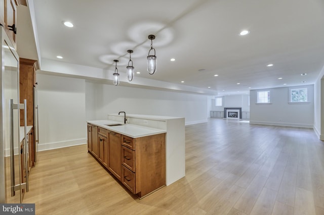 kitchen featuring pendant lighting, a center island with sink, sink, and light hardwood / wood-style floors