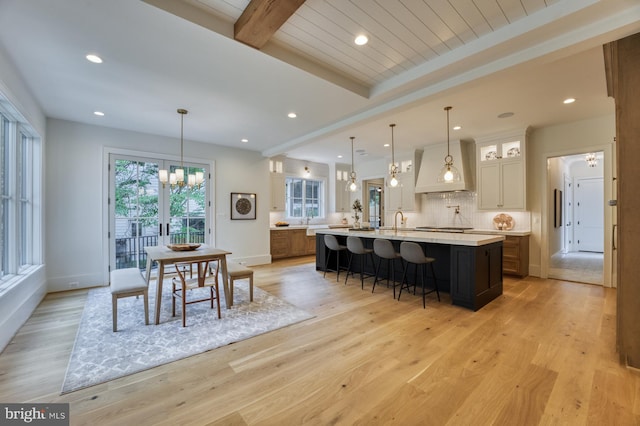 kitchen featuring light hardwood / wood-style flooring, decorative light fixtures, beamed ceiling, premium range hood, and a spacious island