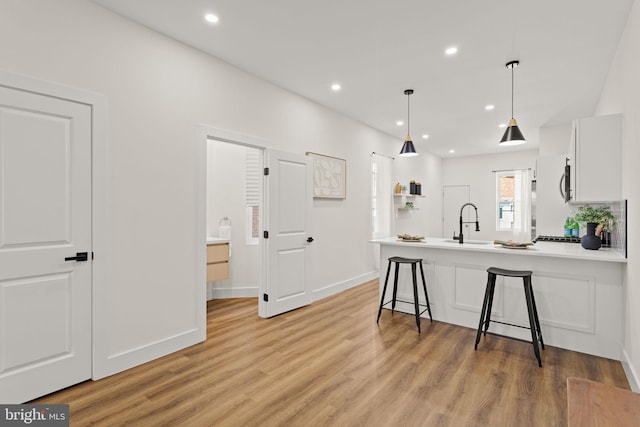 kitchen with a kitchen bar, kitchen peninsula, sink, white cabinetry, and light wood-type flooring