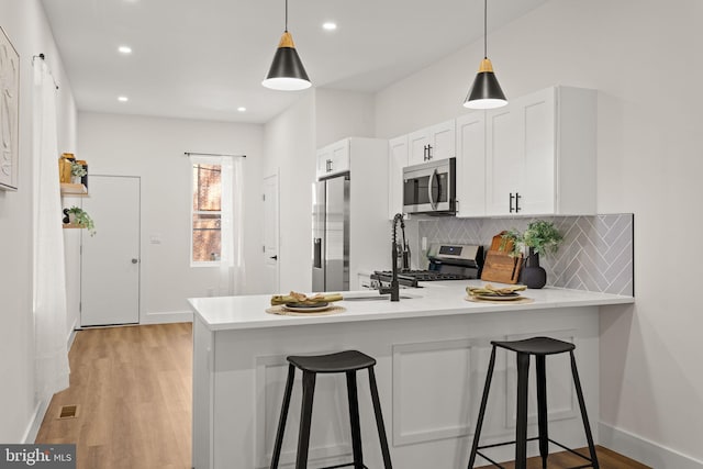 kitchen with appliances with stainless steel finishes, a breakfast bar area, kitchen peninsula, and light hardwood / wood-style flooring