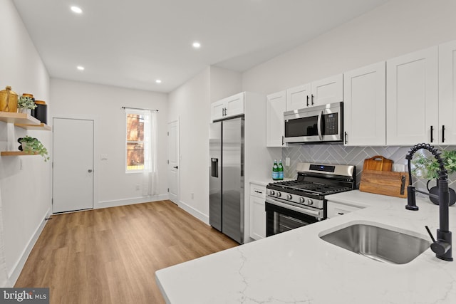 kitchen with light wood-type flooring, stainless steel appliances, light stone counters, sink, and white cabinets