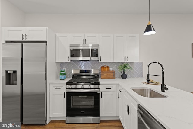 kitchen featuring light stone counters, stainless steel appliances, sink, and decorative light fixtures