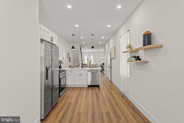 kitchen featuring light wood-type flooring, stainless steel appliances, kitchen peninsula, sink, and white cabinets