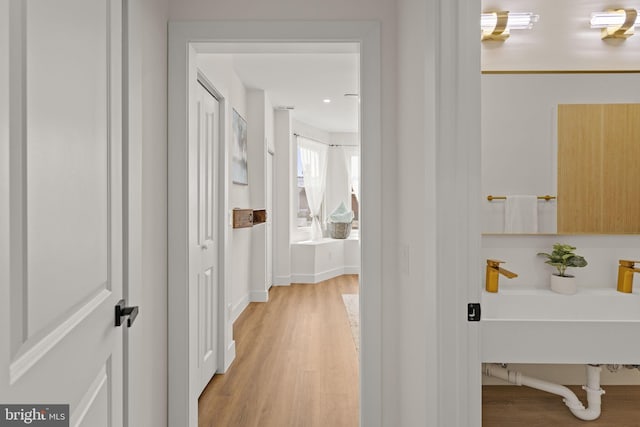 corridor with light wood-type flooring and sink