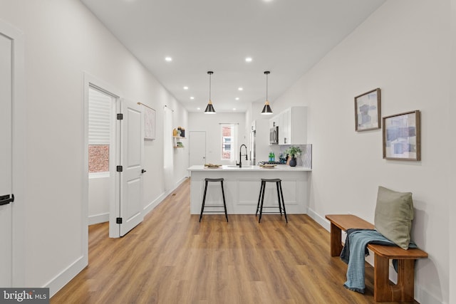 kitchen featuring a breakfast bar, kitchen peninsula, sink, white cabinetry, and light wood-type flooring