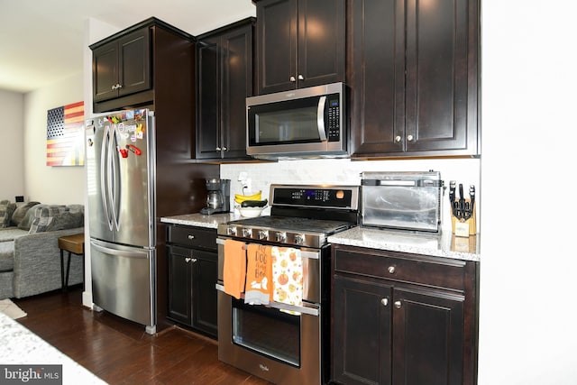 kitchen featuring dark brown cabinetry, tasteful backsplash, light stone counters, dark hardwood / wood-style flooring, and appliances with stainless steel finishes