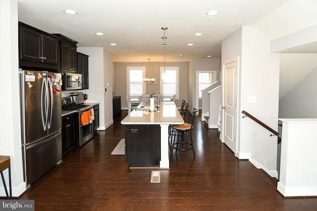 kitchen featuring appliances with stainless steel finishes, dark wood-type flooring, sink, pendant lighting, and a center island with sink