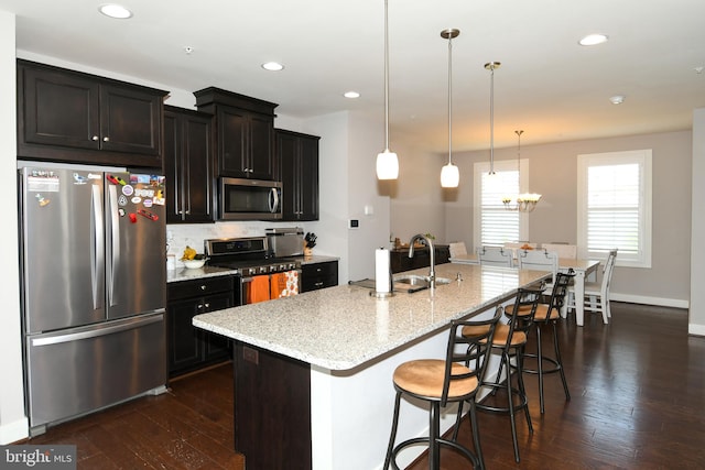 kitchen featuring appliances with stainless steel finishes, dark hardwood / wood-style flooring, light stone counters, pendant lighting, and an island with sink