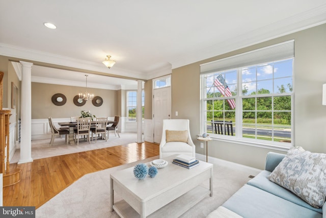 living room featuring light hardwood / wood-style floors, crown molding, decorative columns, and an inviting chandelier