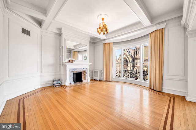 unfurnished living room with visible vents, beam ceiling, an inviting chandelier, a decorative wall, and a premium fireplace