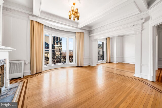 unfurnished living room featuring a fireplace, light wood-type flooring, a notable chandelier, crown molding, and radiator