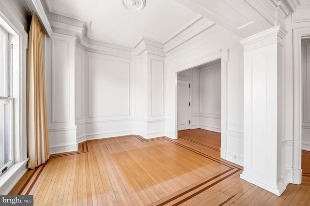 empty room featuring hardwood / wood-style floors, a decorative wall, ornate columns, and ornamental molding