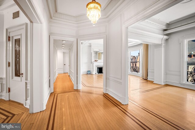 hallway featuring crown molding, light hardwood / wood-style flooring, and an inviting chandelier