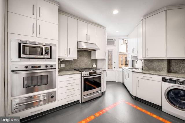 kitchen with under cabinet range hood, decorative backsplash, appliances with stainless steel finishes, washer / clothes dryer, and a warming drawer