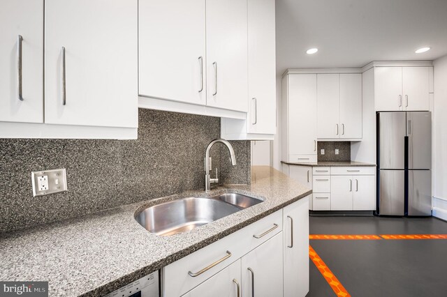 kitchen with white cabinetry, backsplash, stainless steel refrigerator, and sink