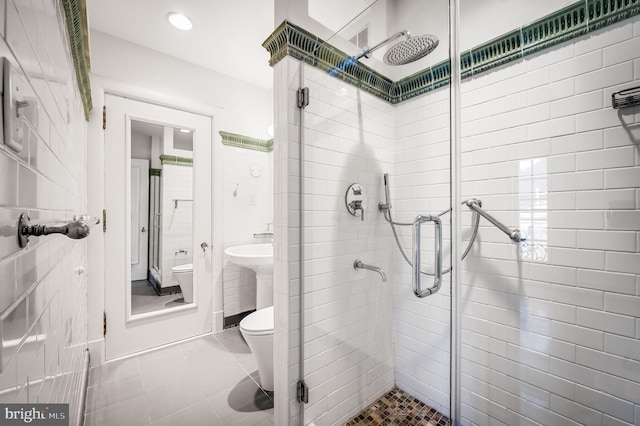 full bath with toilet, a stall shower, a sink, tile walls, and tile patterned flooring