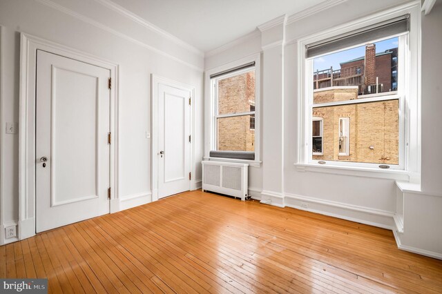 empty room with radiator heating unit, ornamental molding, and light hardwood / wood-style flooring