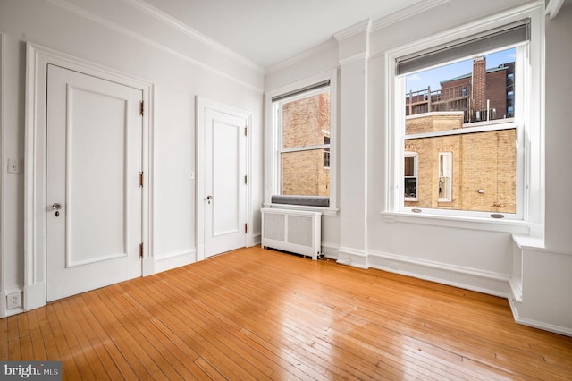 unfurnished bedroom with crown molding, radiator heating unit, baseboards, and hardwood / wood-style floors