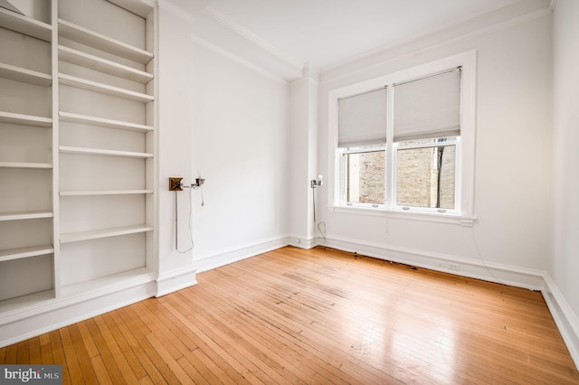 empty room featuring built in features, ornamental molding, baseboards, and hardwood / wood-style floors