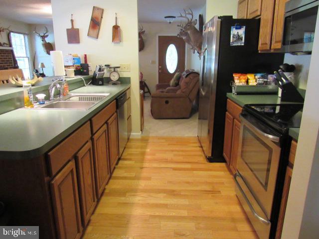 kitchen with appliances with stainless steel finishes, kitchen peninsula, sink, and light hardwood / wood-style floors