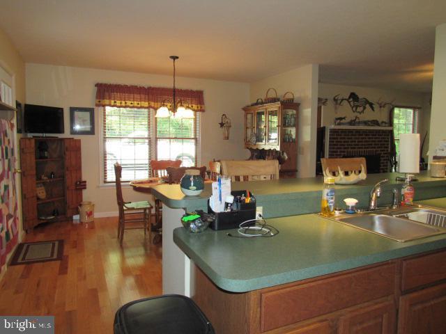 kitchen featuring a fireplace, light wood-type flooring, a notable chandelier, sink, and pendant lighting